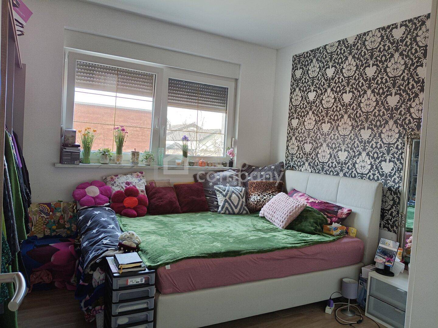 Gemütliches Schlafzimmer mit gemusterter Tapete, großem Fenster und viel Tageslicht.