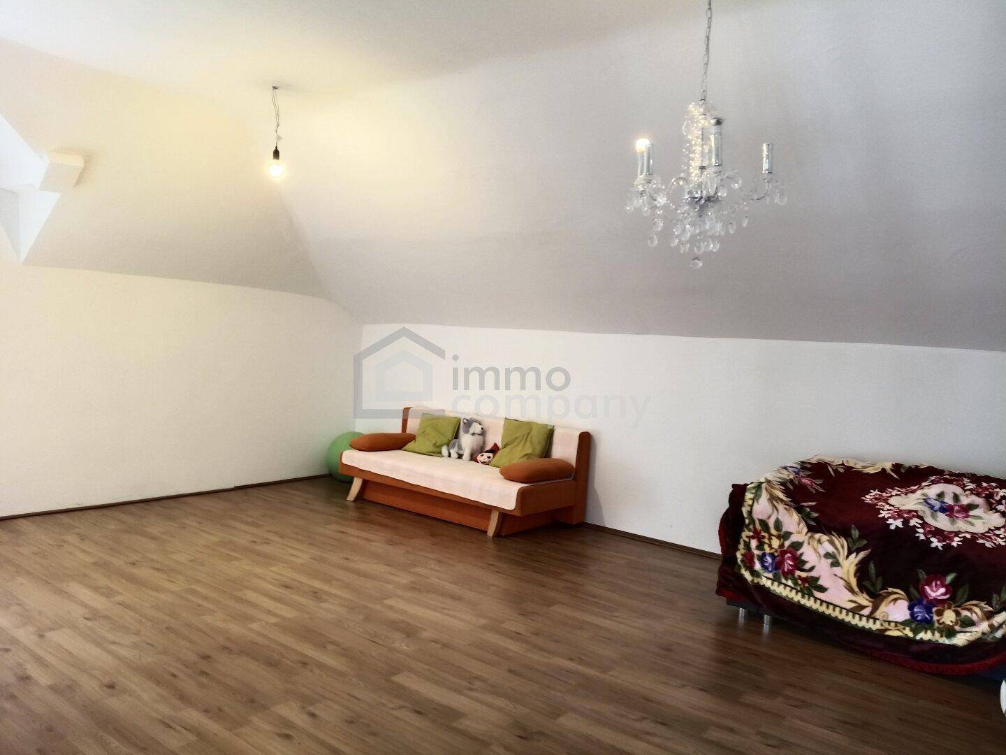 Geräumiger Dachbodenraum mit Holzboden, schrägen Wänden und Kronleuchter.