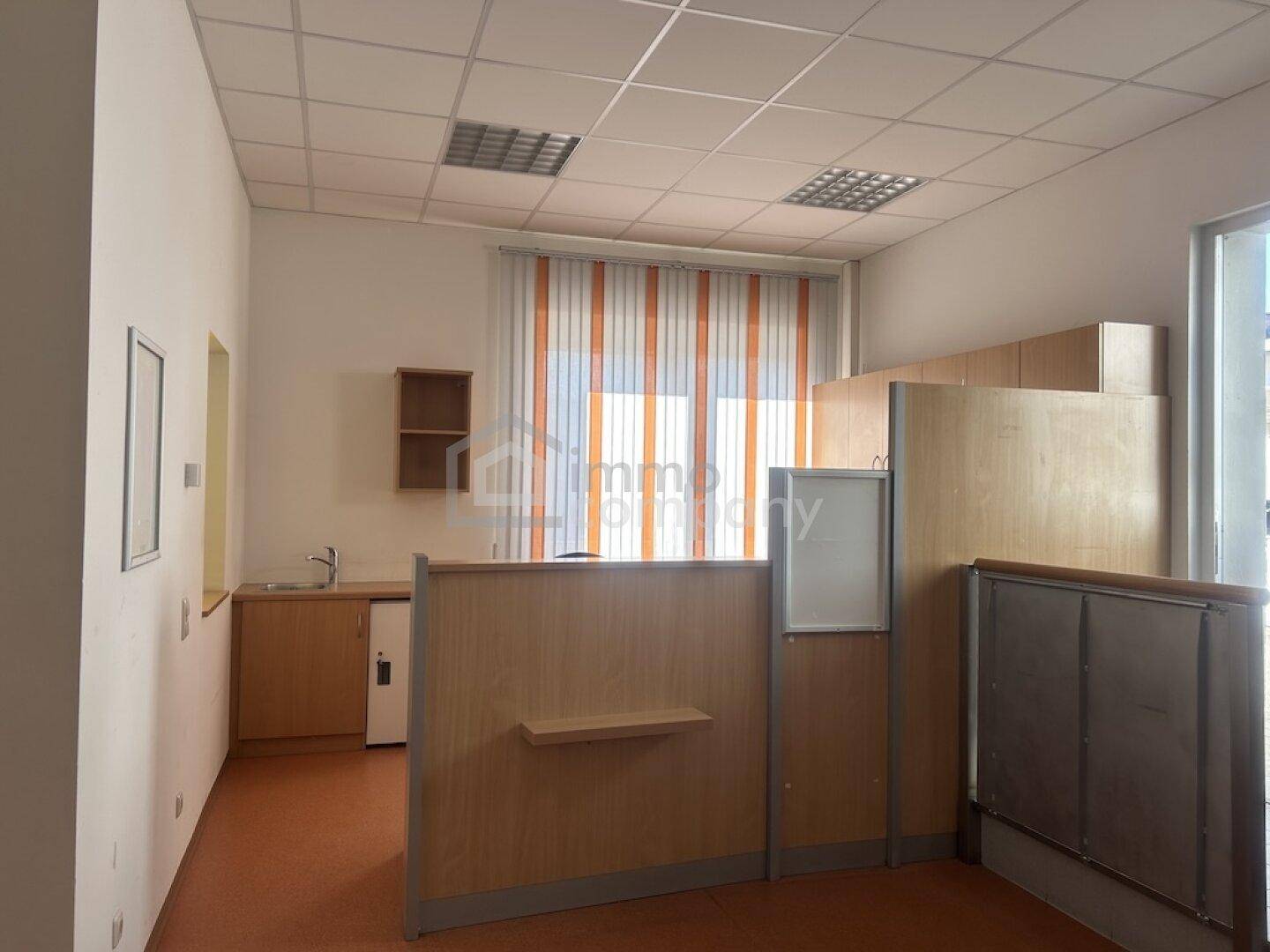 Offener Bürobereich mit kleiner Küchenzeile, Trennwänden und Deckenbeleuchtung.