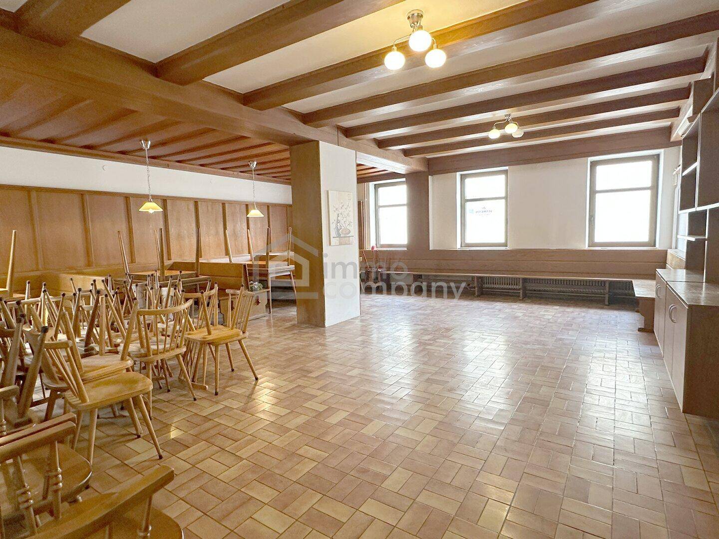 Großer Saal mit Holzbalkendecke und Fliesenboden, ideal für Veranstaltungen und Feiern.
