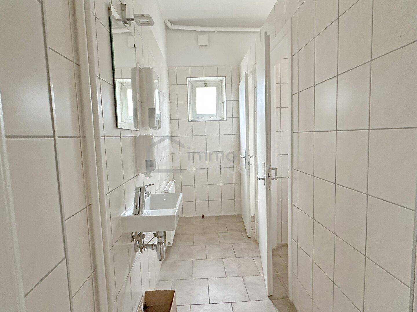 Heller Sanitärbereich mit weißen Fliesen, Waschbecken und Spiegeln, gut gepflegt.