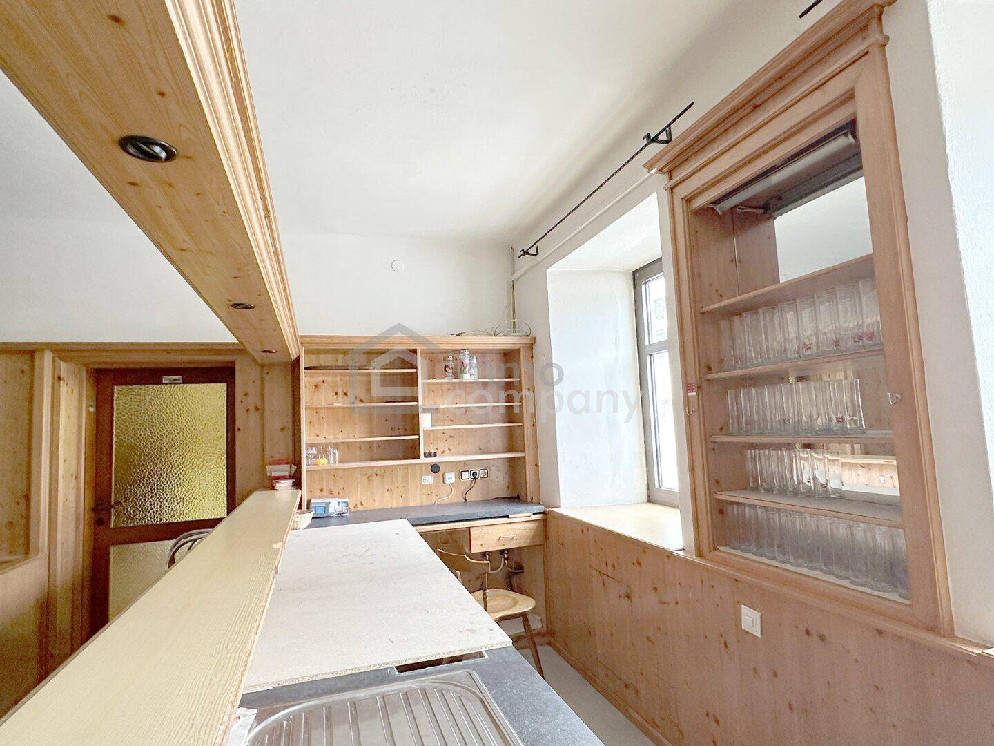Kleine Theke mit Spüle und Holzregalen, ideal für eine Bar oder einen Ausschankbereich.