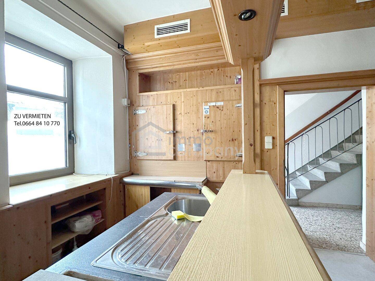 Rustikaler Ausschankbereich mit Holzverkleidung, Spüle und Blick auf eine Treppe.