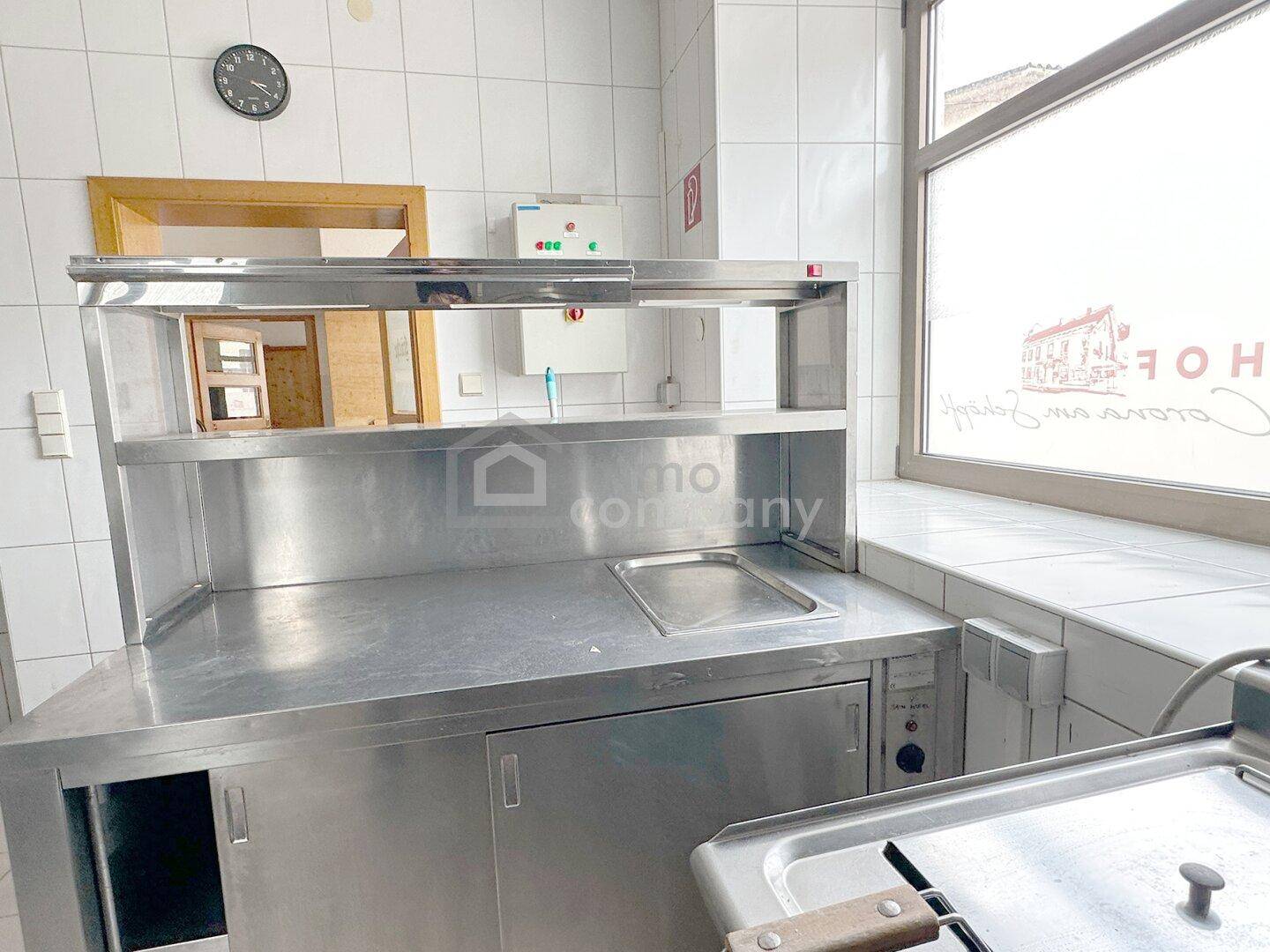 Edelstahl-Arbeitsbereich in einer Großküche mit Spüle und Ablageflächen, gut beleuchtet.