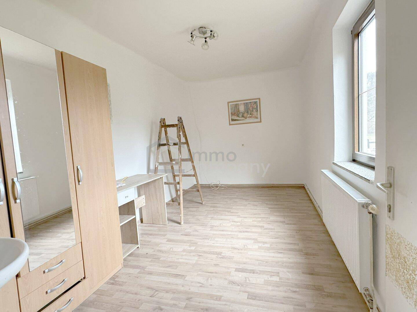 Helles Schlafzimmer mit Laminatboden, Fenster und einem Kleiderschrank, unmöbliert.