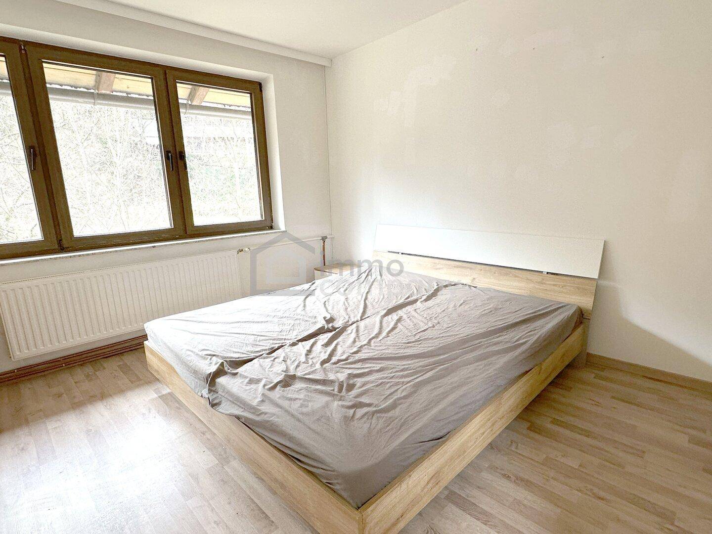 Helles Schlafzimmer mit Doppelbett, Laminatboden und großen Fenstern, gemütlich eingerichtet.