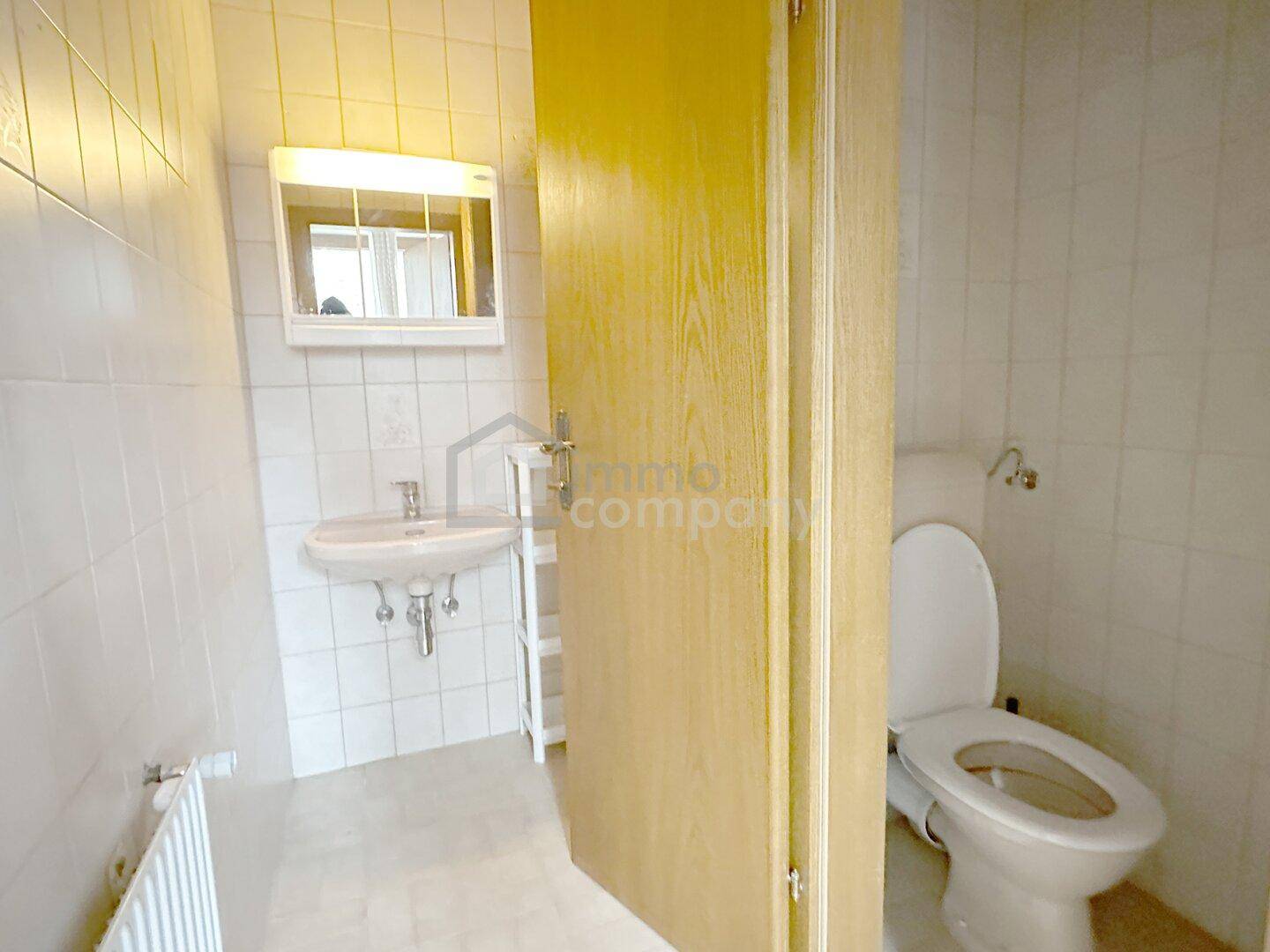 Kleines Badezimmer mit weißen Fliesen, Waschbecken und Toilette, funktional und hell.