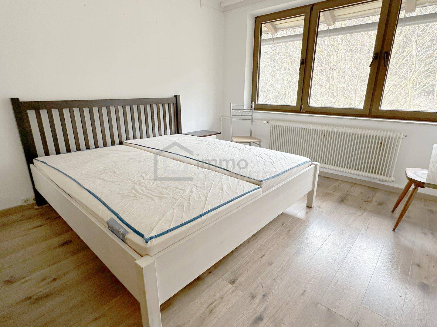 Helles Schlafzimmer mit zwei Einzelbetten, Laminatboden und großen Fenstern, einfach eingerichtet.