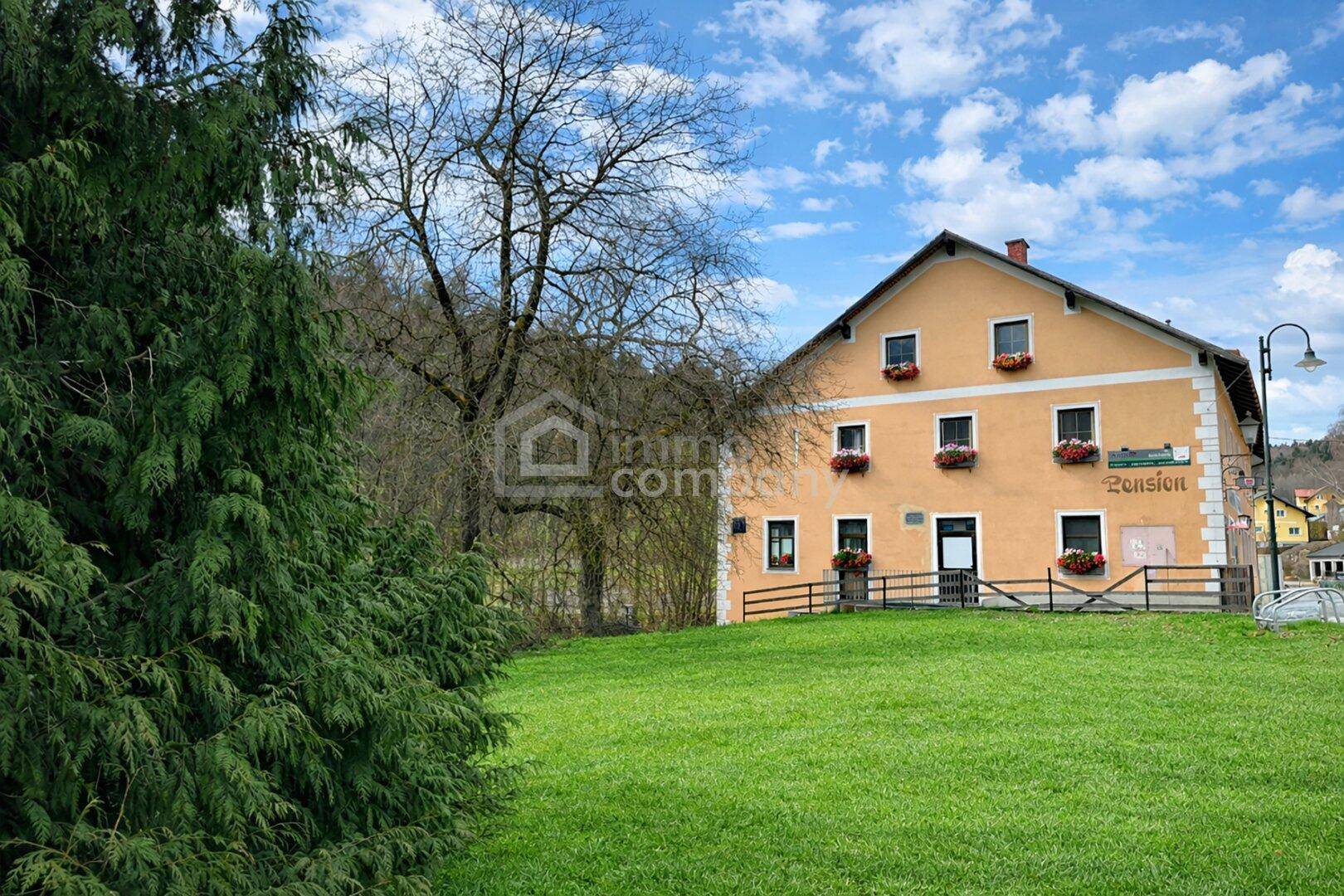 Gelb gestrichenes historisches Gebäude mit grüner Wiese und Bäumen im ländlichen Umfeld.