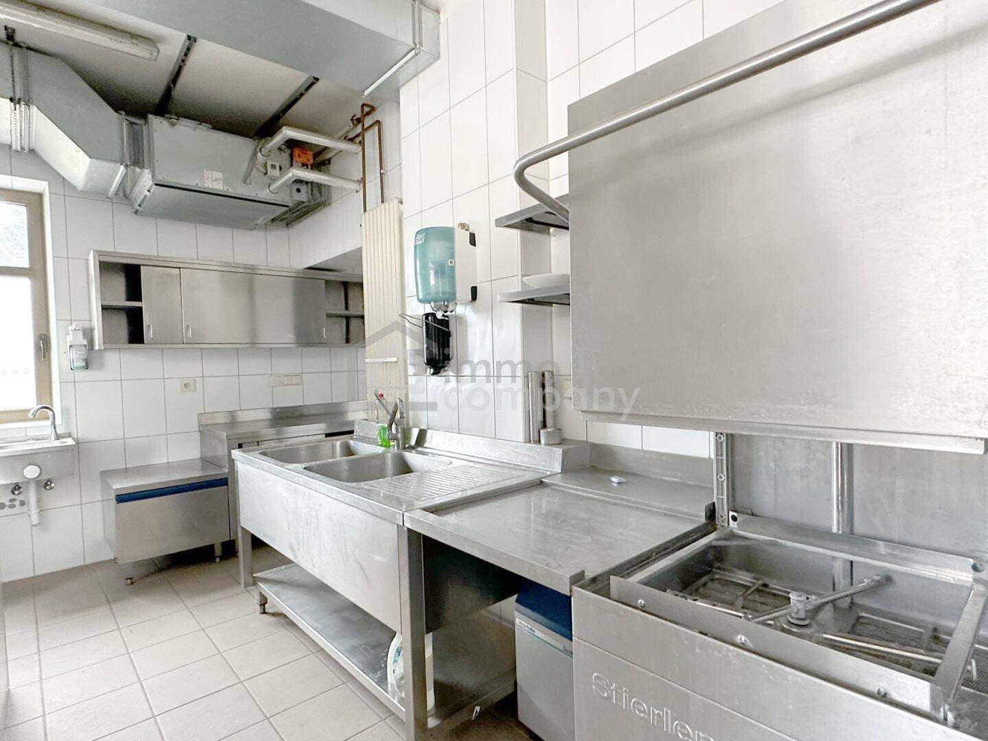 Großküche mit professioneller Spülmaschine, Edelstahl-Arbeitsflächen und Ablagen.