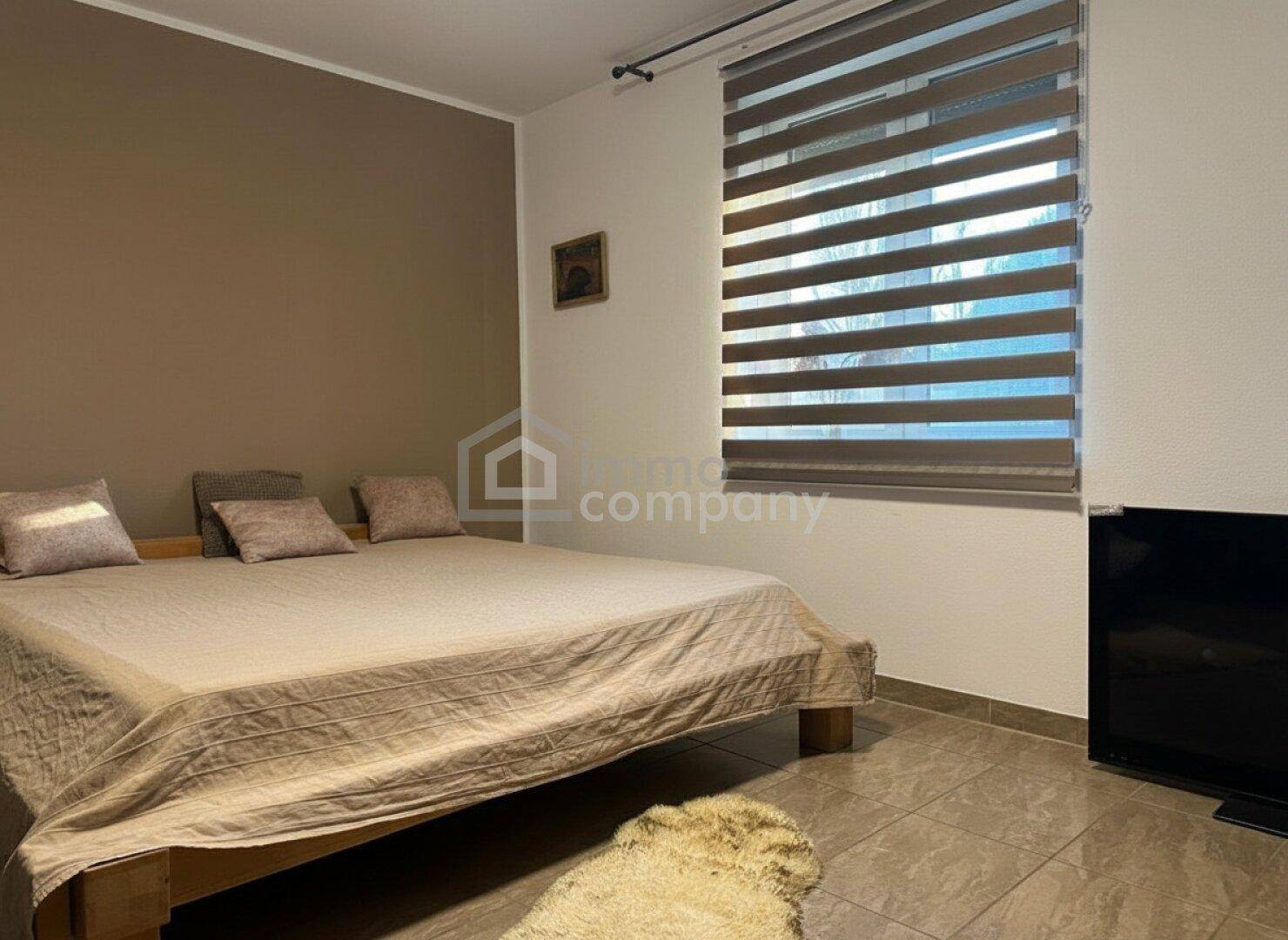 Gemütliches Schlafzimmer mit großem Bett, Fliesenboden und Fenster mit Jalousien.