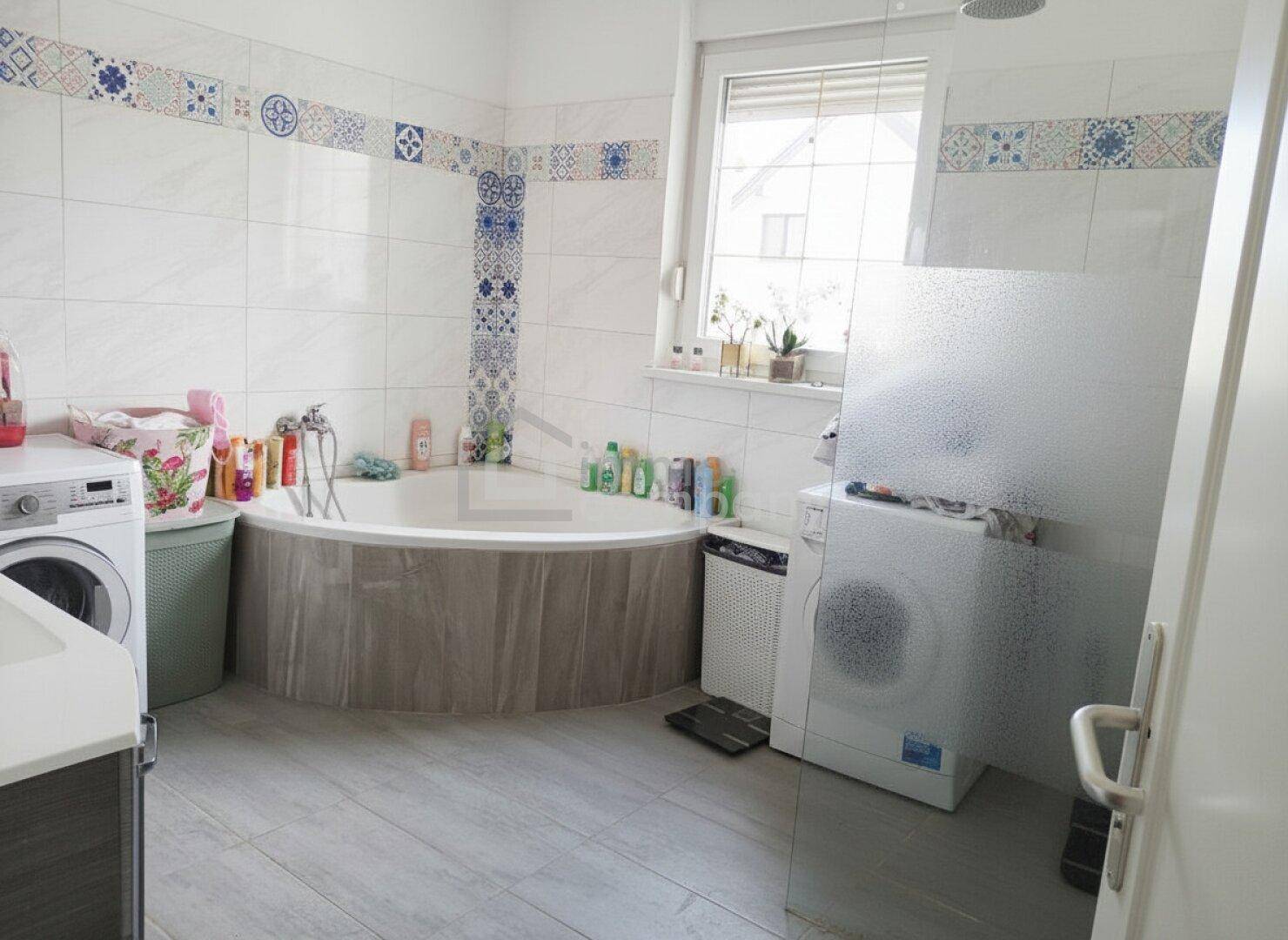 Geräumiges Badezimmer mit Badewanne, Dusche, Waschmaschine und Fenster.