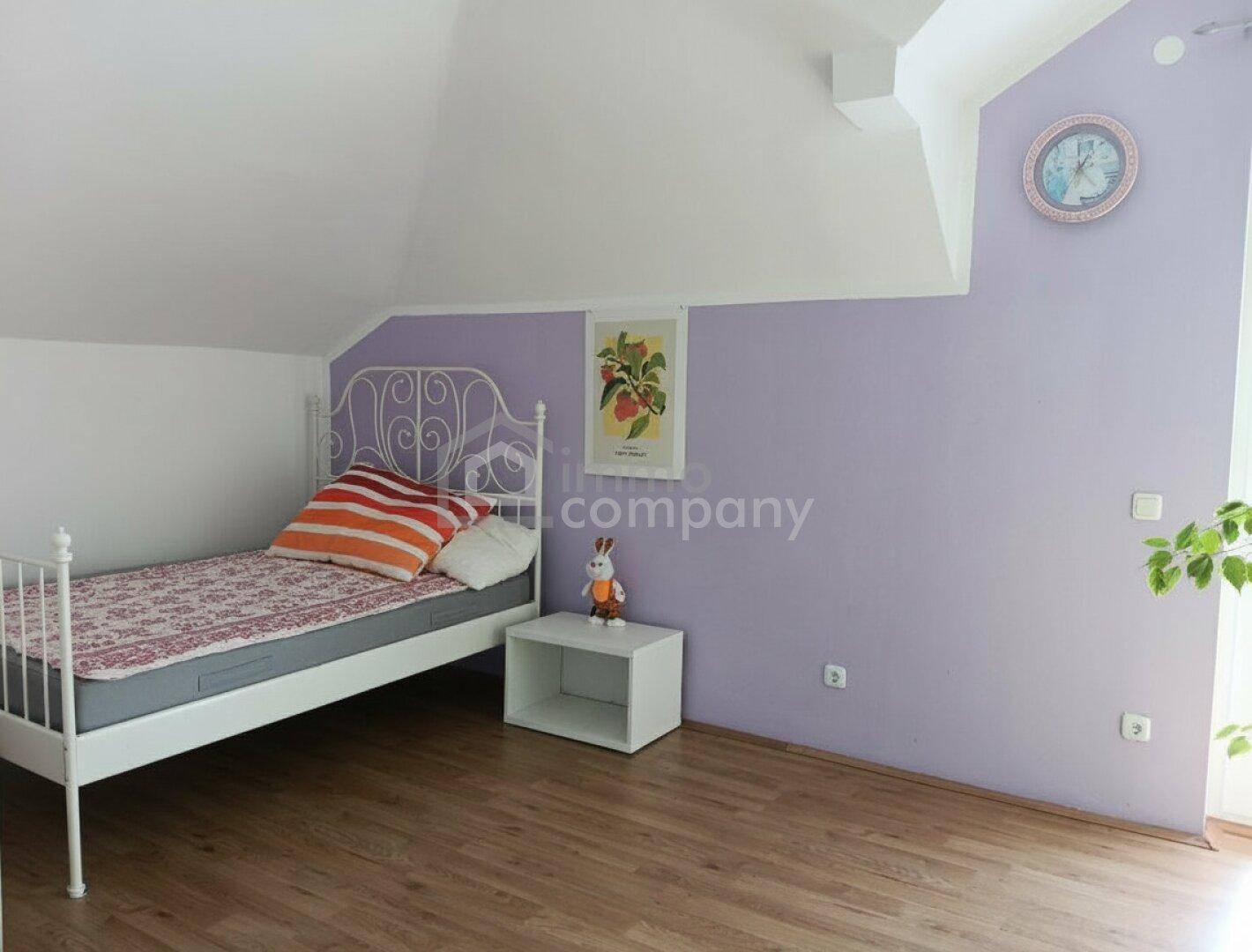 Helles Schlafzimmer im Dachgeschoss mit Holzboden, lila Wand und schrägen Decken.