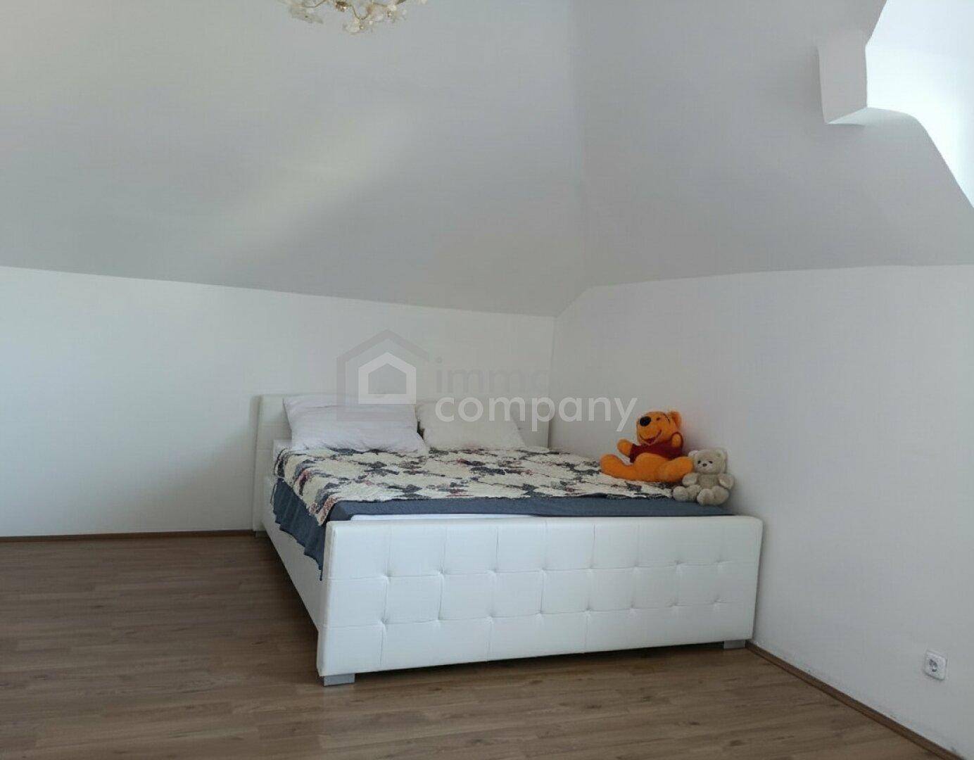 Schlafzimmer im Dachgeschoss mit weißem Bett, Holzboden und schrägen Wänden.