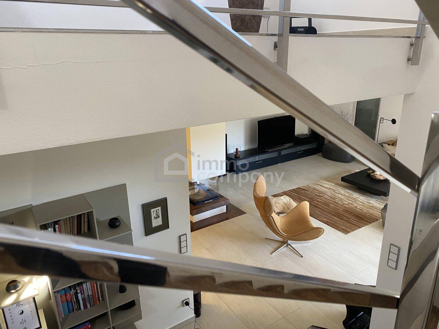 Blick von der Galerie in den offenen Wohnbereich mit modernen Möbeln und hellem Fliesenboden.