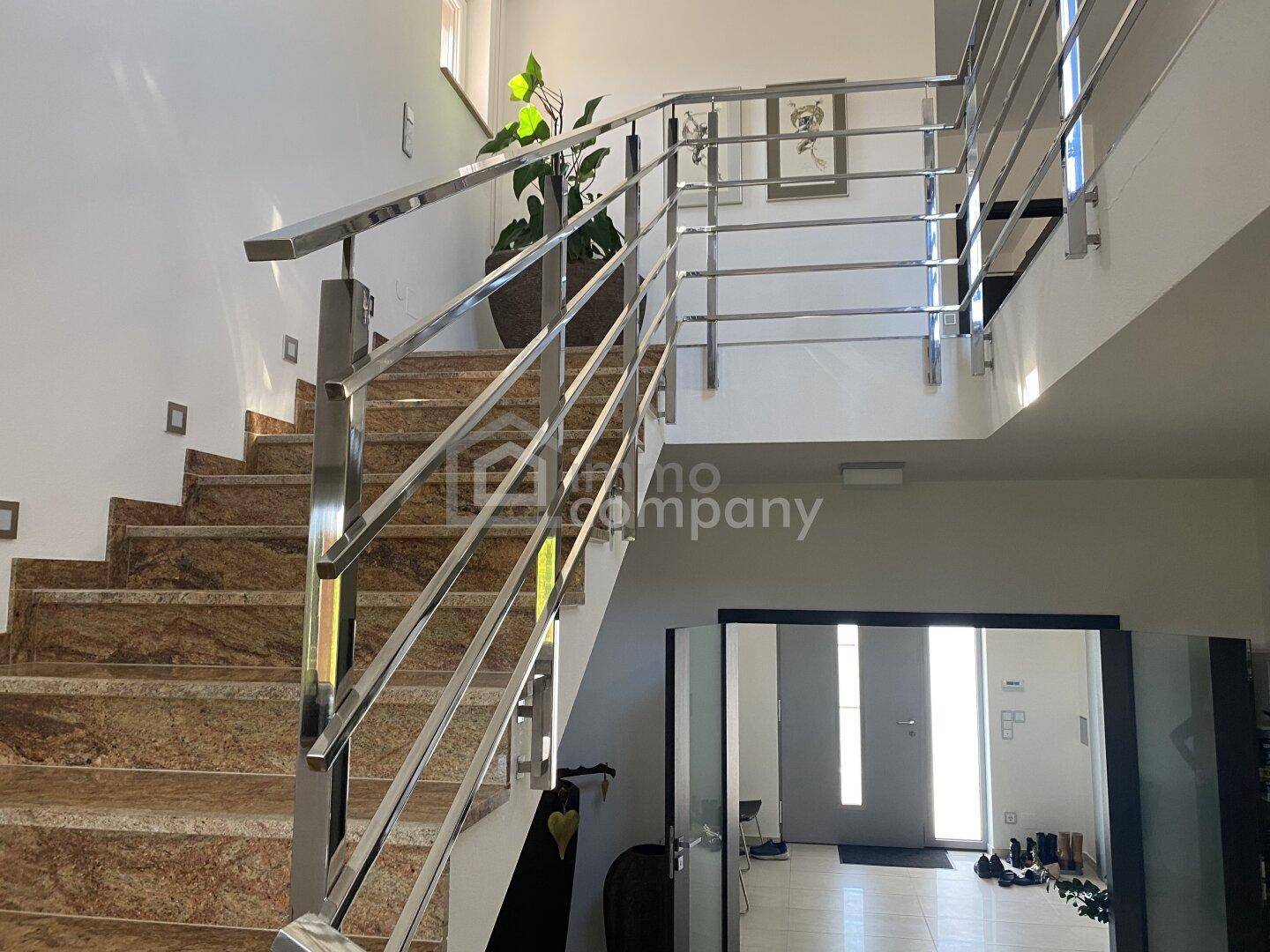 Elegante Treppe mit Marmorstufen und modernem Edelstahlgeländer, die zum Eingangsbereich führt.
