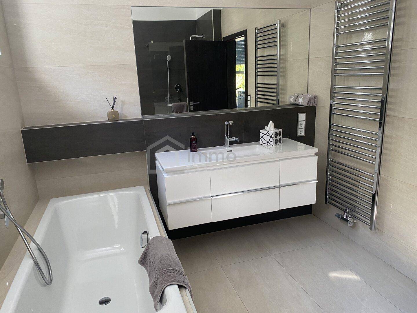 Modernes Badezimmer mit Badewanne, großem Spiegel, Einzelwaschbecken und beheiztem Handtuchhalter.