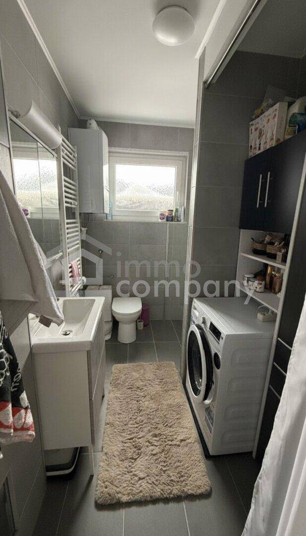 Modernes Badezimmer mit Dusche, WC, Waschbecken und Waschmaschine, hell beleuchtet.