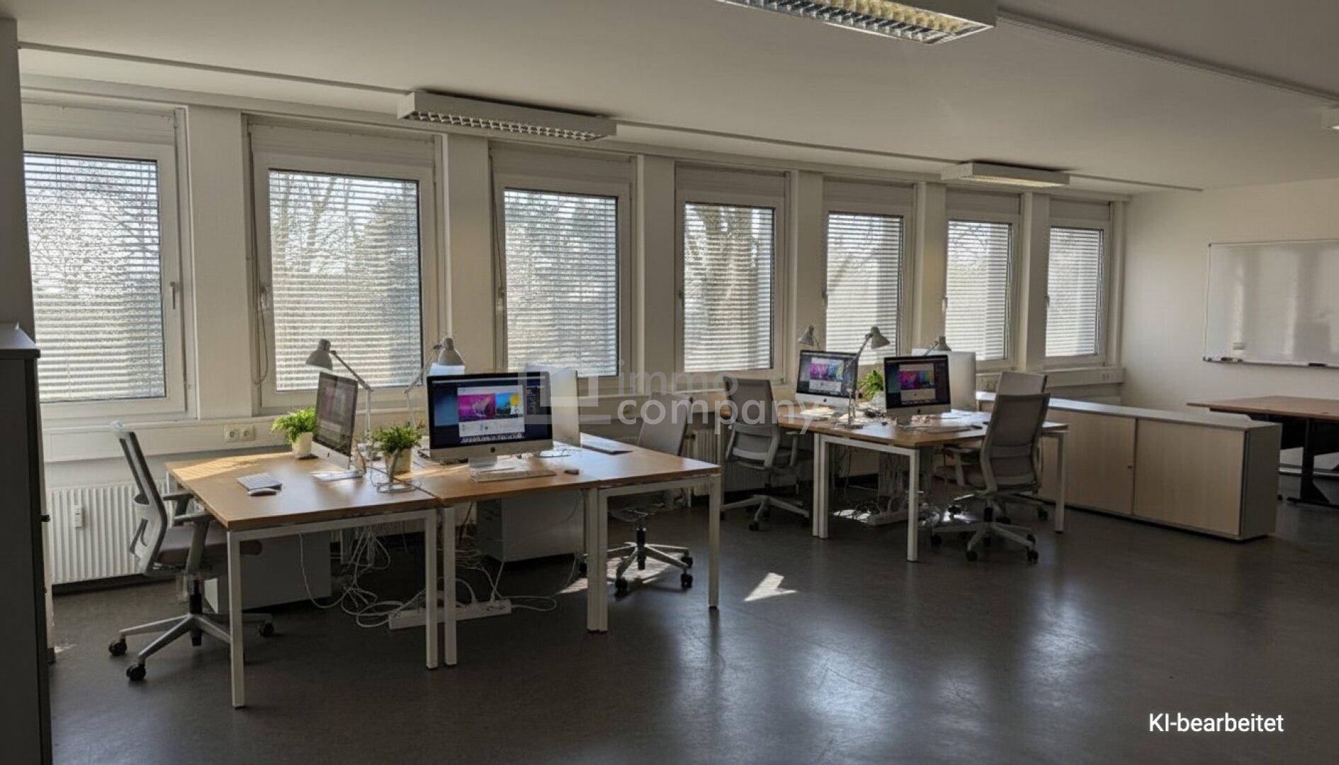 Helles Großraumbüro mit mehreren Arbeitsplätzen, großen Fenstern und einem Whiteboard für Präsentationen.