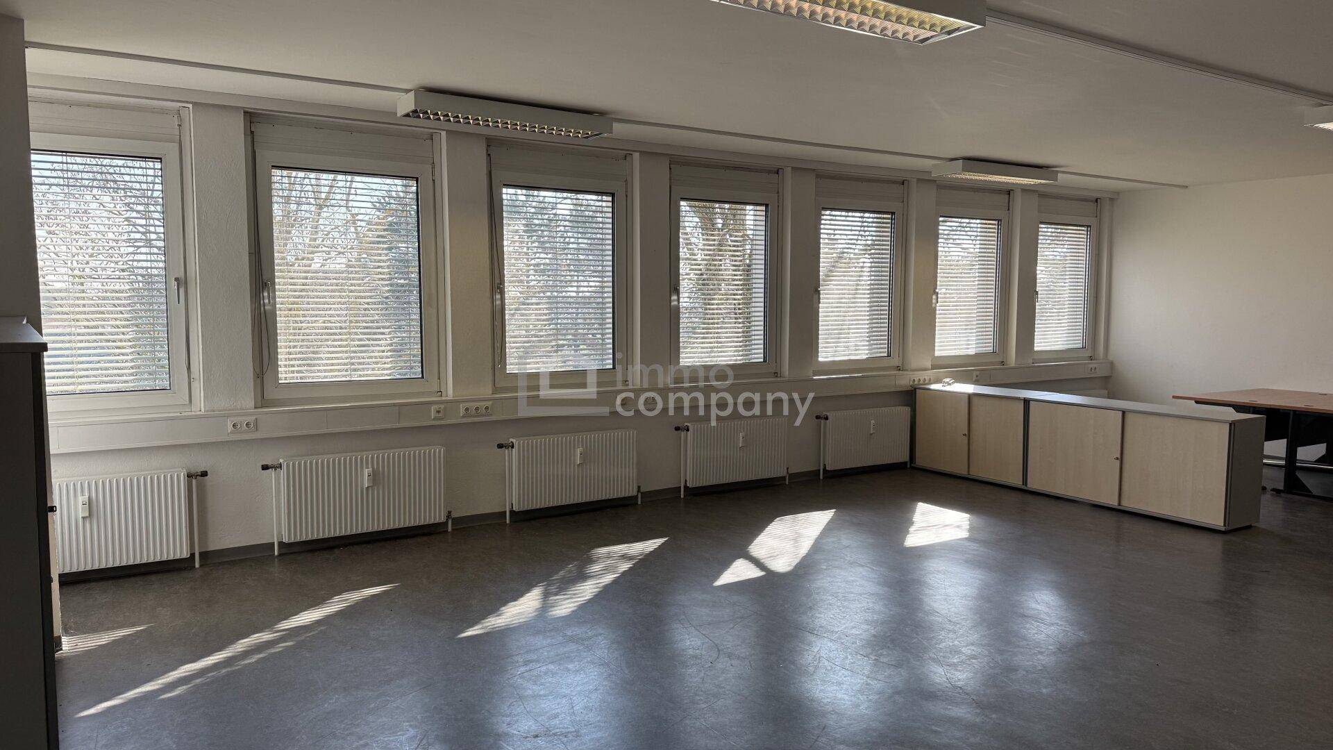 Leeres Büro mit einer Reihe von Fenstern, Heizkörpern und einem niedrigen Sideboard für Stauraum.