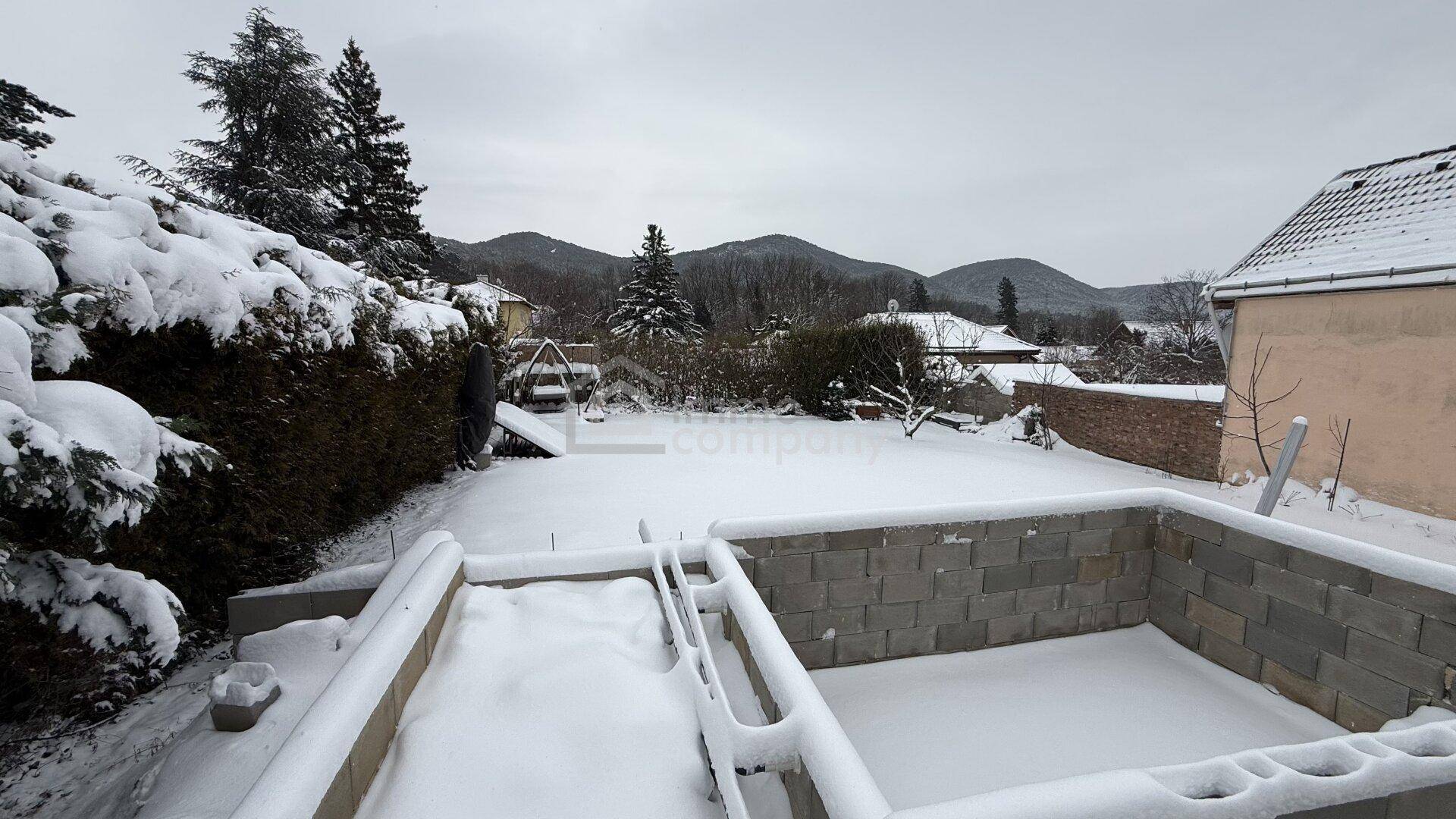 Winterlicher Gartenbereich mit Schneedecke und Blick auf die umliegende Berglandschaft.