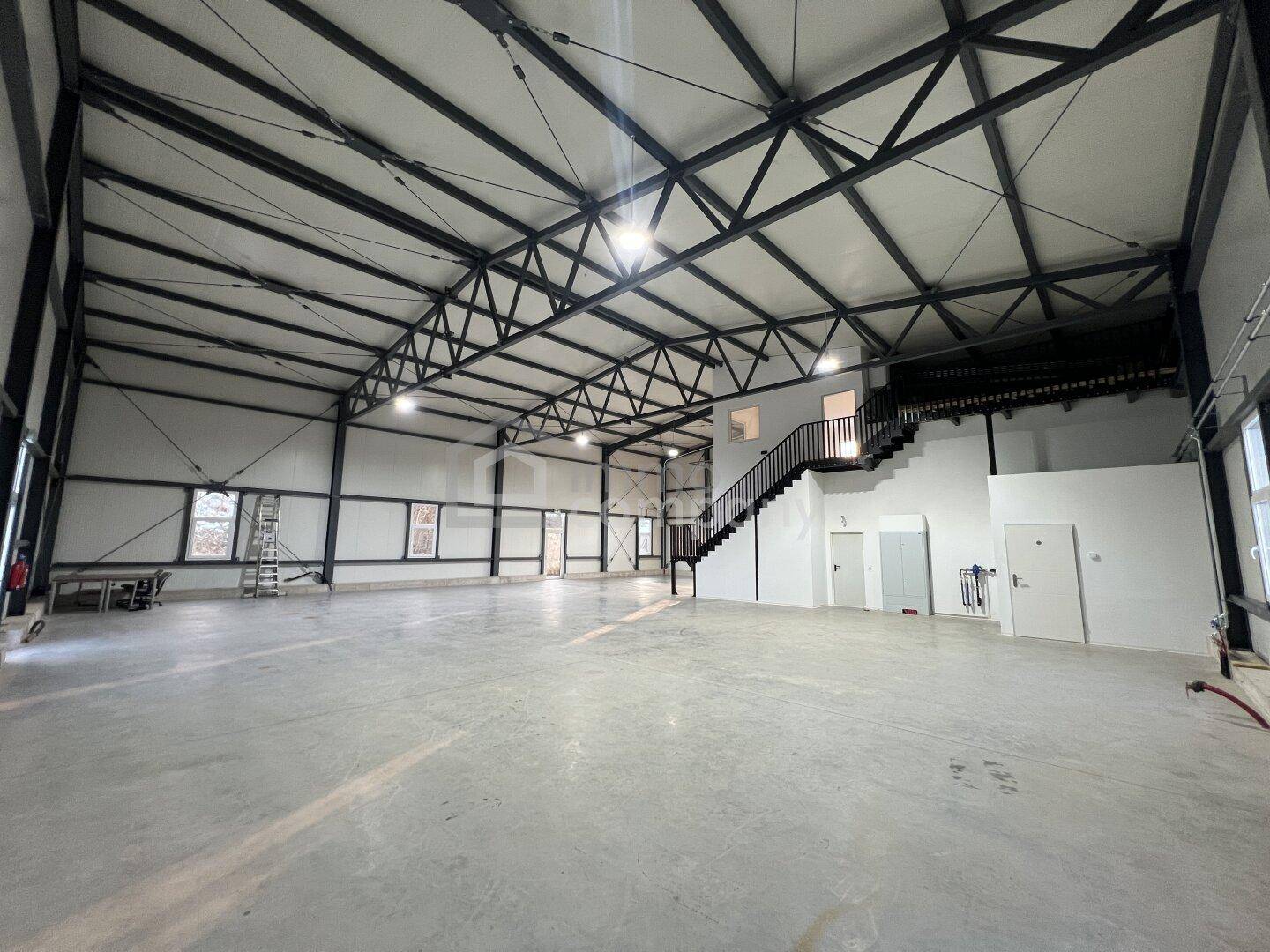 Weitläufige, leere Industriehalle mit hoher Decke, sichtbarer Stahlkonstruktion und Betonboden, bereit zur Nutzung.
