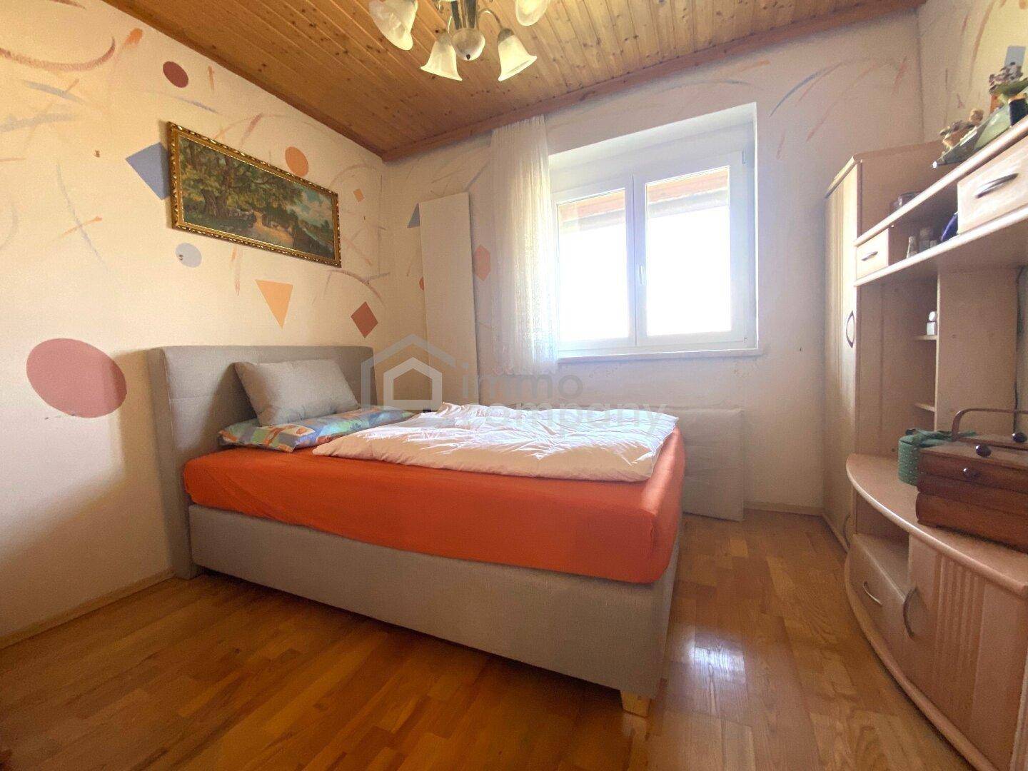 Kinderzimmer mit Einzelbett, Holzdecke und farbenfroher Wandgestaltung, hell durch das Fenster.