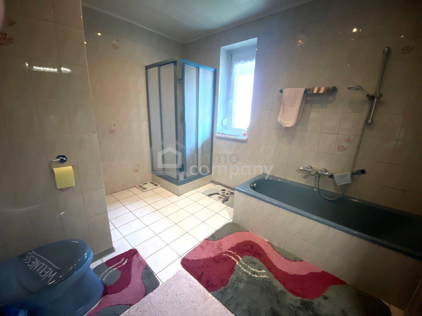 Badezimmer mit Badewanne, Duschkabine, WC und Fenster, im älteren Stil gehalten.