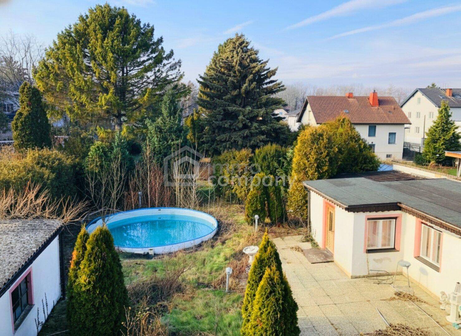 Hinterhof mit einem Aufstellpool, Terrasse und umgebenden Bäumen und Sträuchern.
