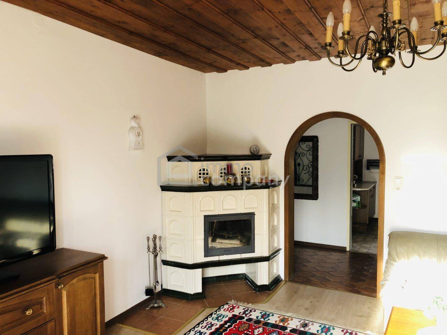 Wohnbereich mit Kachelofen, Holzbalkendecke und Zugang zur Küche.