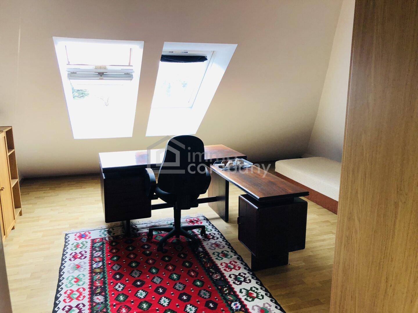 Arbeitszimmer im Dachgeschoss mit Schreibtisch, Teppich und Dachfenstern.