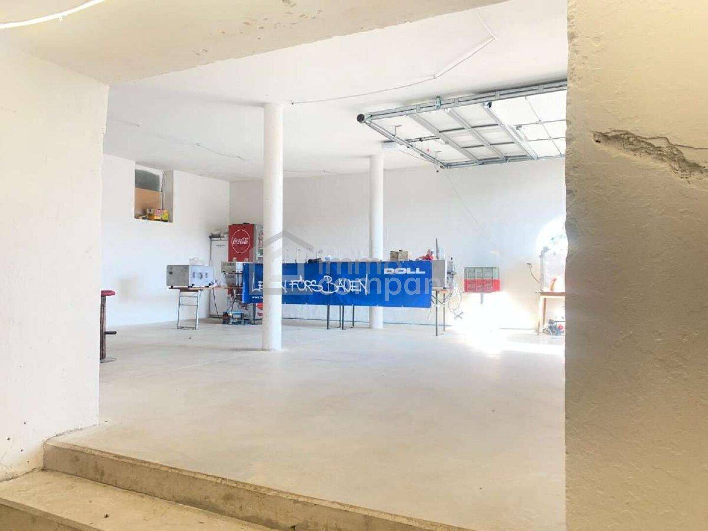 Vielseitiger Kellerraum mit Garagentor und einer Bar, geeignet für Veranstaltungen oder als Werkstatt.