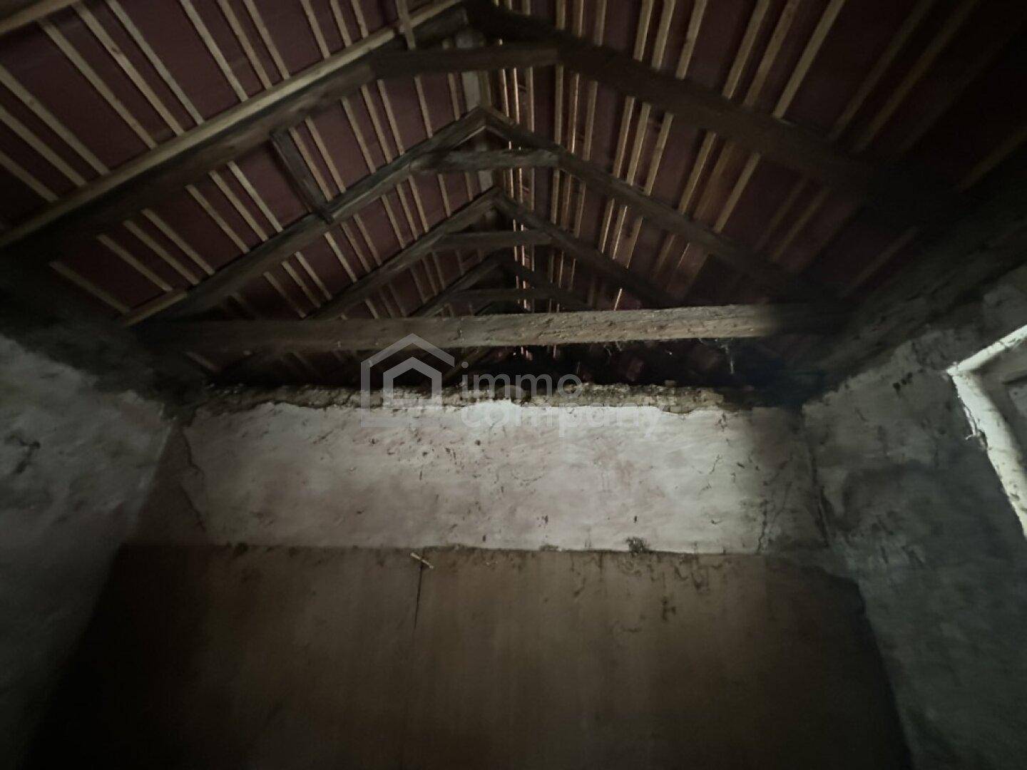 Innenansicht eines baufälligen Raumes mit sichtbarer Dachkonstruktion und unverputzten Wänden.