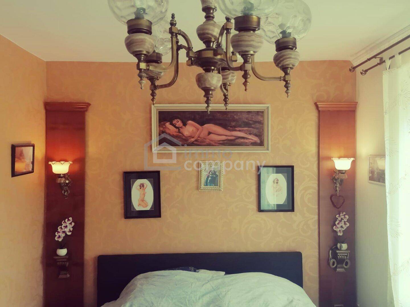Schlafzimmer mit goldener Tapete, klassischem Kronleuchter und dekorativen Wandleuchten.