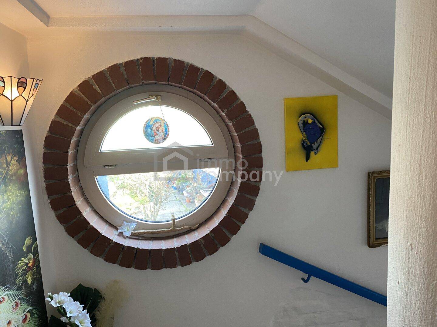 Treppenhaus mit einem markanten runden Fenster, umgeben von Ziegeln, das viel Licht hereinlässt.