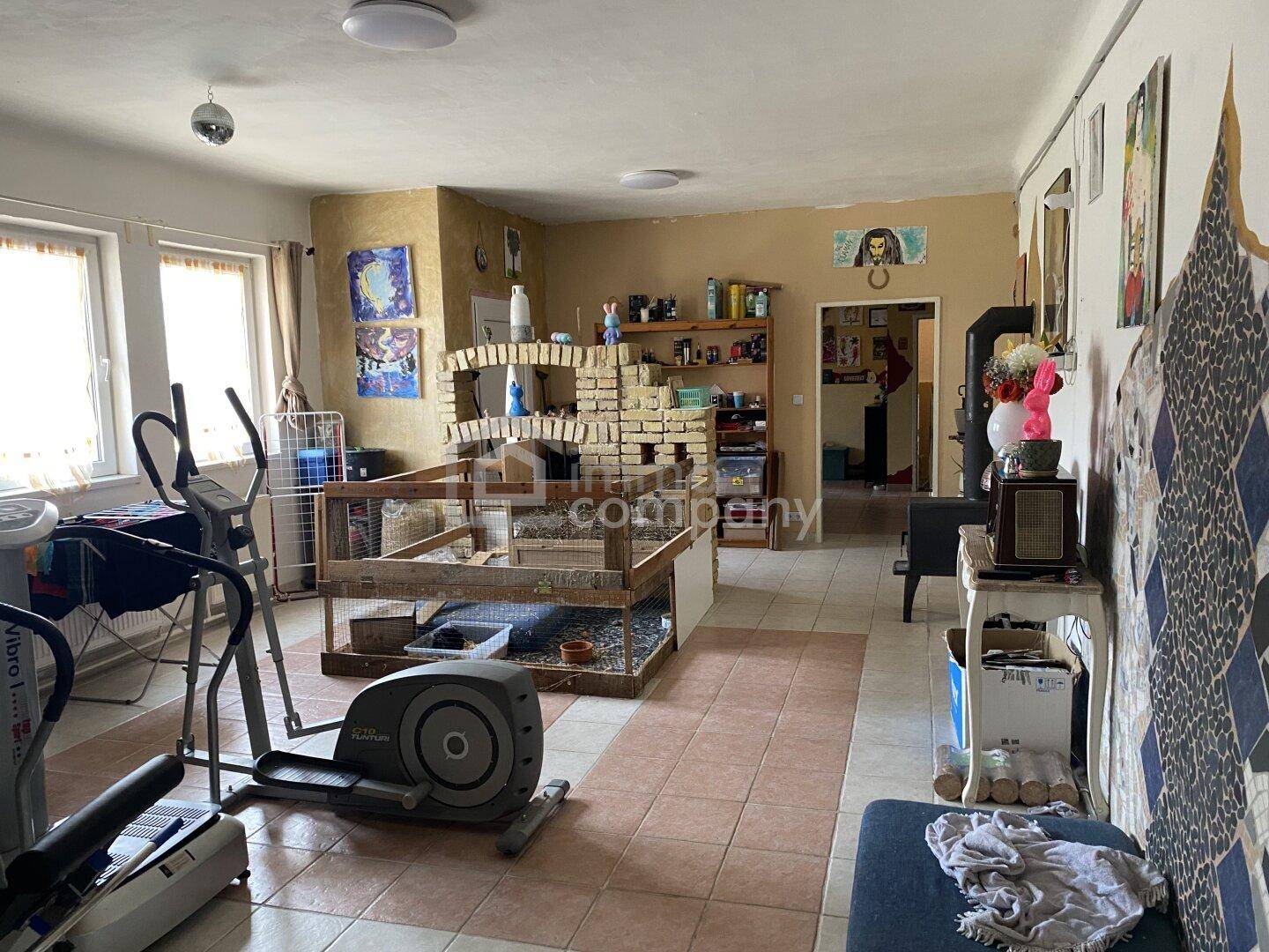 Vielseitiger Wohnraum mit Fitnessgeräten, Ziegelstrukturen und einem Kaminofen im Hintergrund.