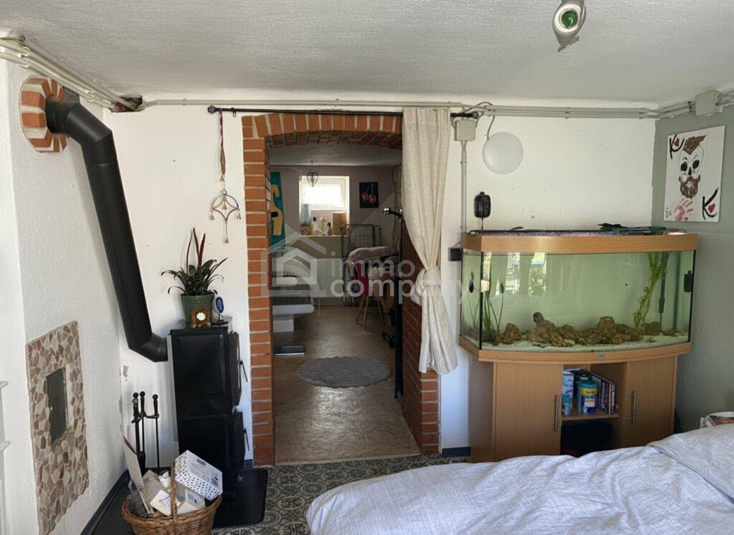 Schlafzimmer mit Kaminofen, Aquarium und Ziegelbogen als Übergang zu einem weiteren Raum.