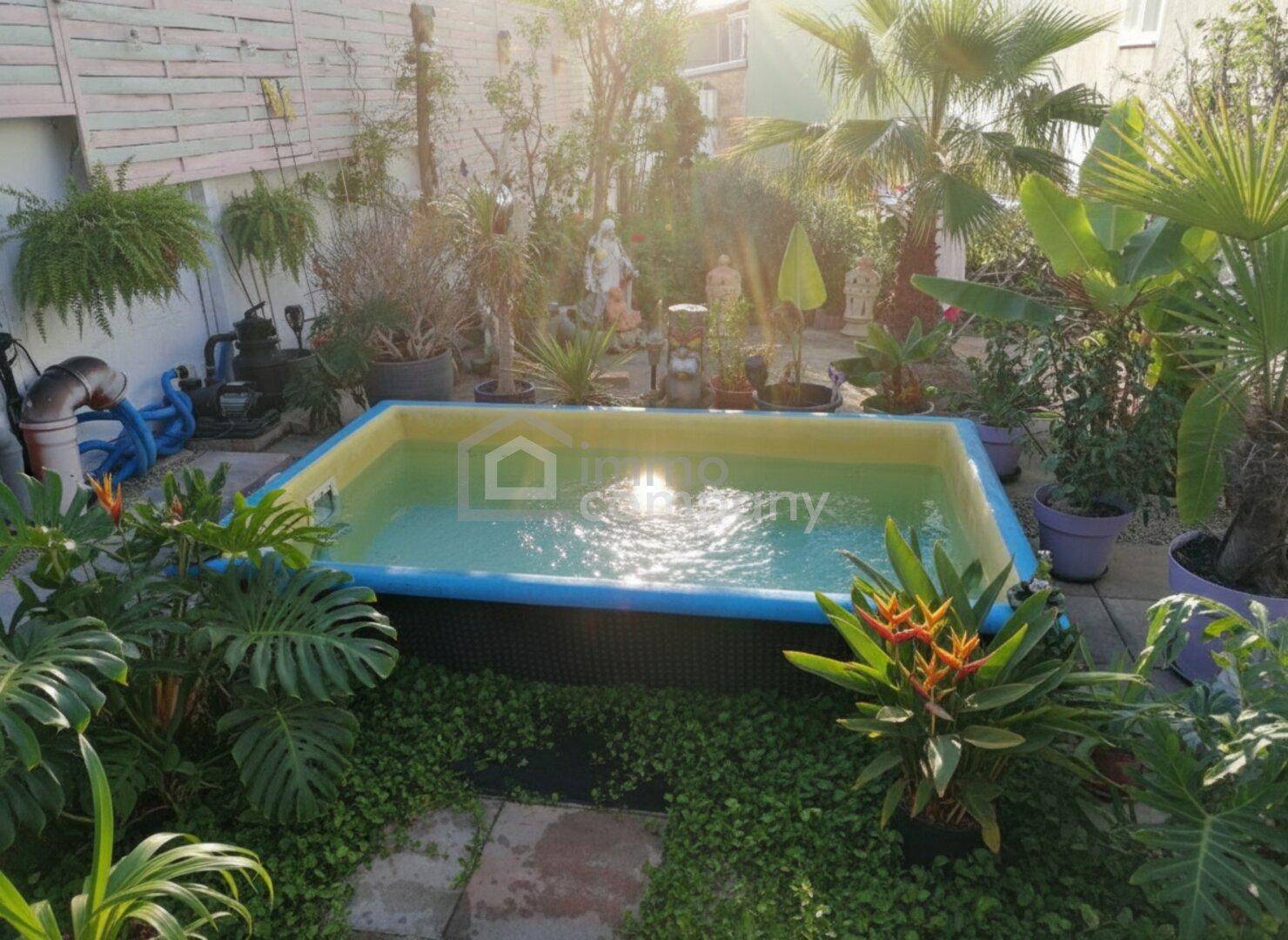Tropischer Garten mit einem Aufstellpool, üppiger Vegetation und viel Sonnenlicht.