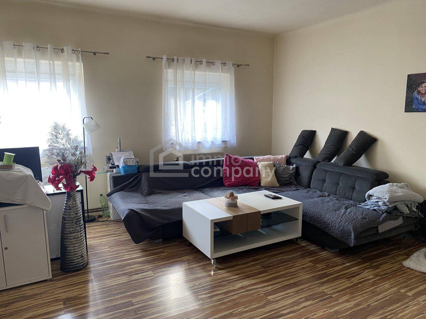 Gemütliches Wohnzimmer mit großem Ecksofa, Laminatboden und viel Tageslicht durch die Fenster.
