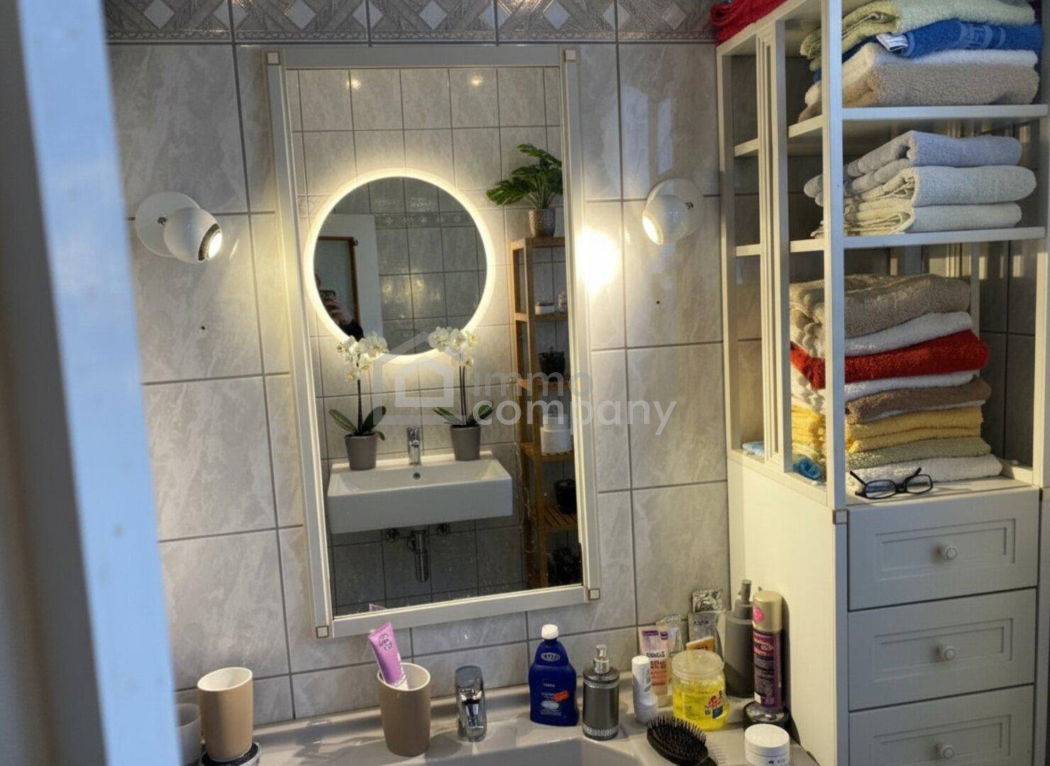 Helles Badezimmer mit modernem Waschbecken, beleuchtetem Spiegel und praktischen Regalen.
