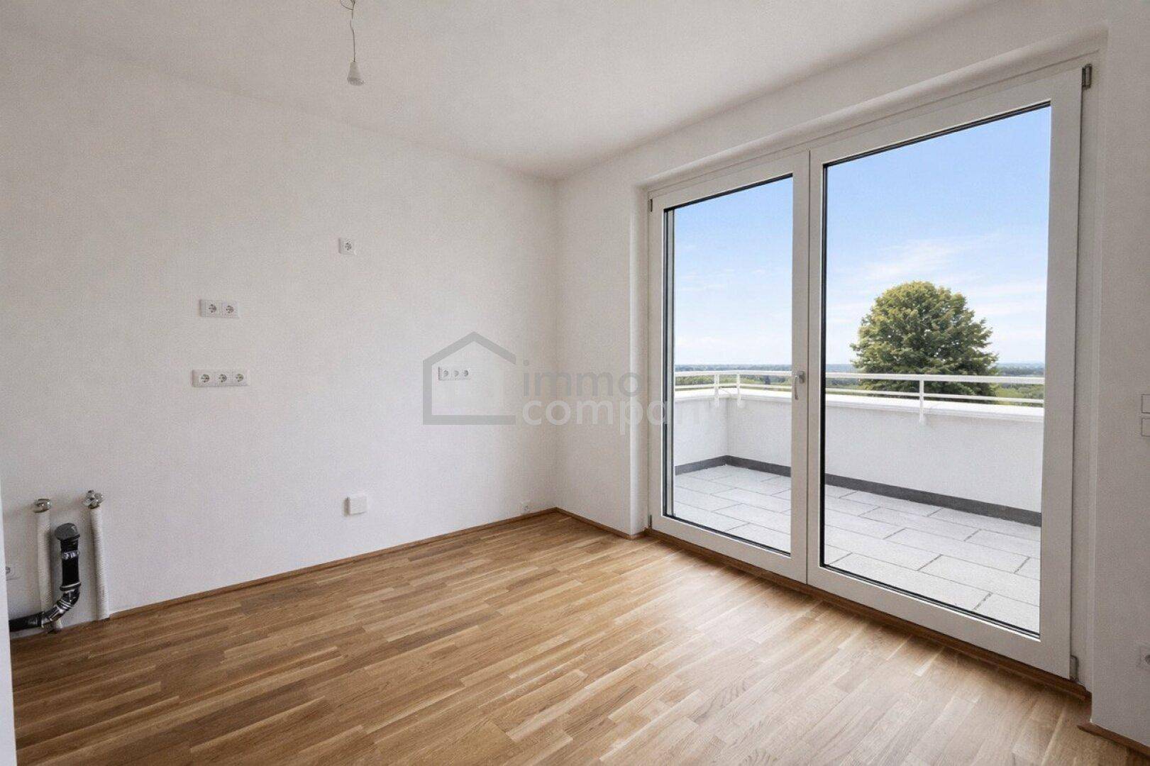 Heller Raum mit Parkettboden und großem Fenster, das Zugang zu einer Terrasse bietet.
