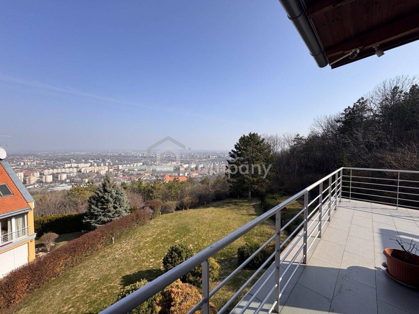 Geräumige Terrasse mit Metallgeländer und weitem Blick über die Stadt und grüne Hügel.