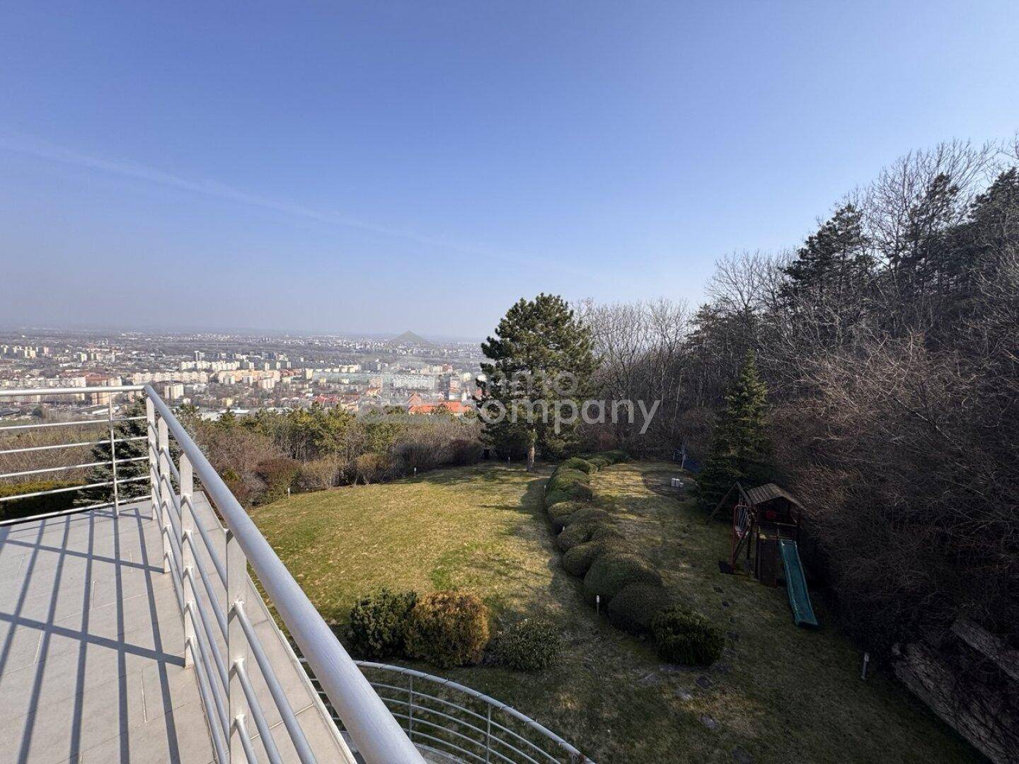 Großer Gartenbereich mit Rasenfläche, Büschen und einem kleinen Spielplatz mit Stadtpanorama.