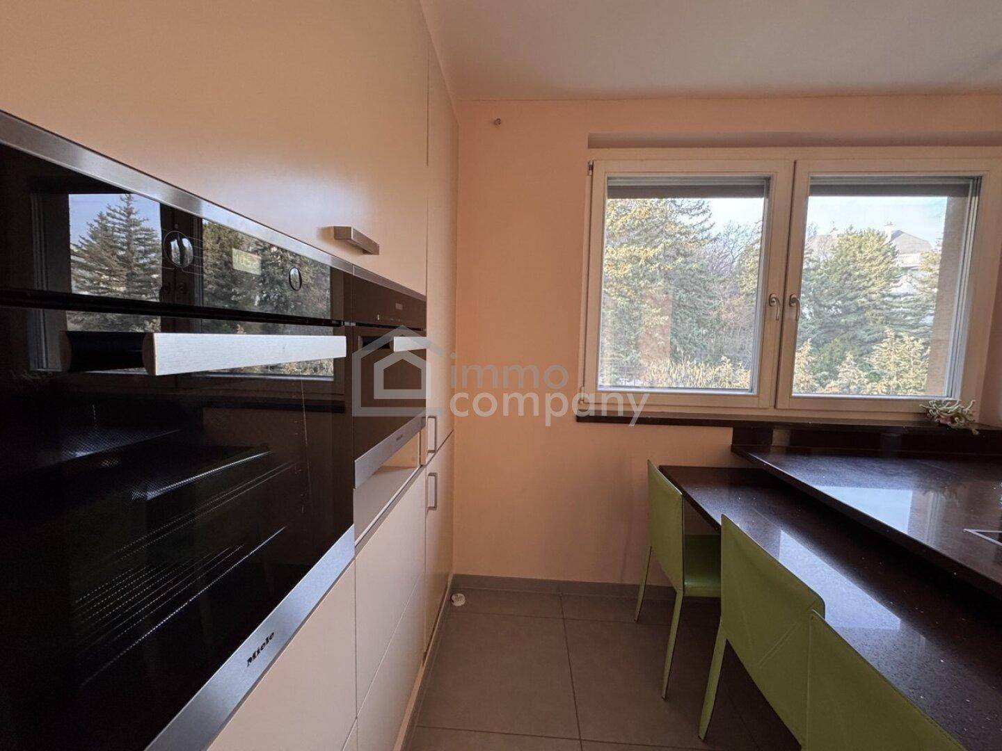 Moderne Küche mit Einbaugeräten, Fenster und dunkler Arbeitsplatte mit Blick ins Grüne.