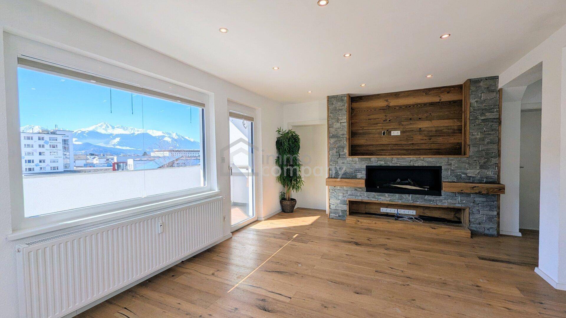 Helles Wohnzimmer mit Holzboden, modernem Kamin und beeindruckendem Bergblick durch große Fenster.