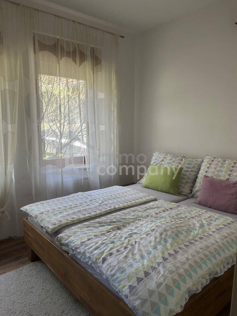 Helles Schlafzimmer mit Doppelbett, Vorhängen und Blick ins Grüne.