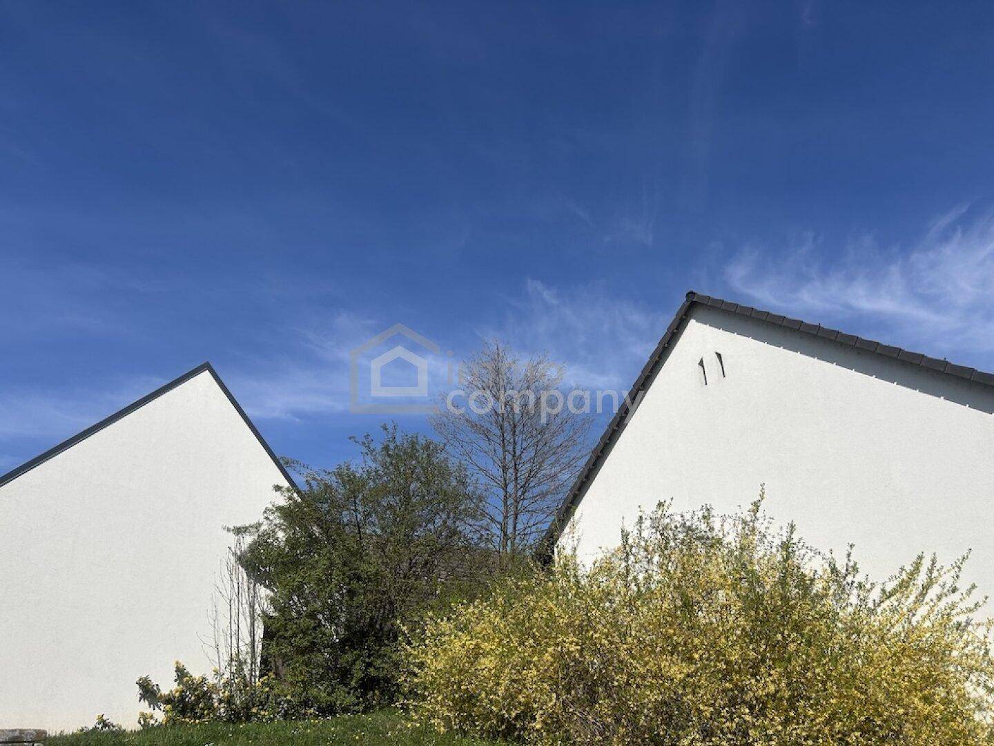 Zwei weiße Giebelwände mit Satteldächern unter einem strahlend blauen Himmel.