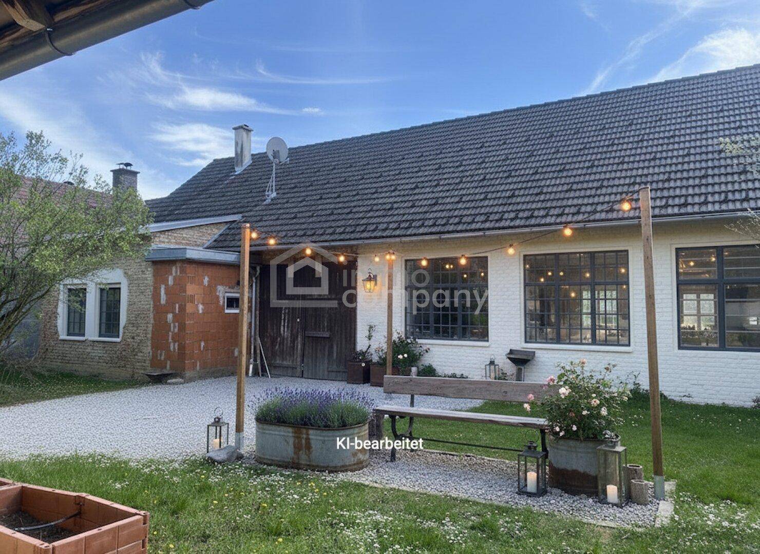 Gemütlicher Gartenbereich mit Lichterkette, Sitzbank und Pflanzen vor der renovierten Fassade.