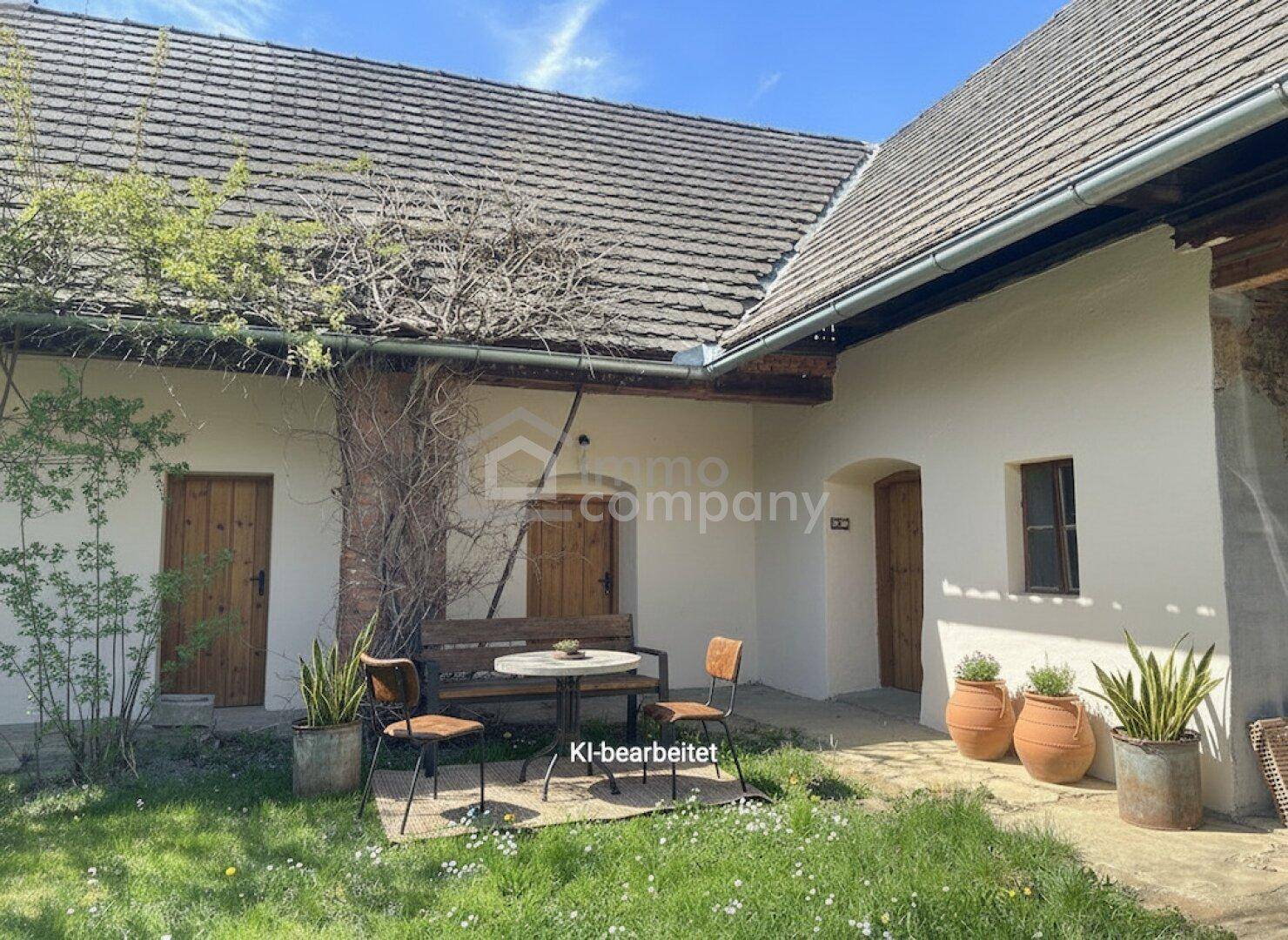 Renovierter Innenhof mit weiß getünchten Wänden, Holztüren und gemütlicher Sitzgelegenheit.