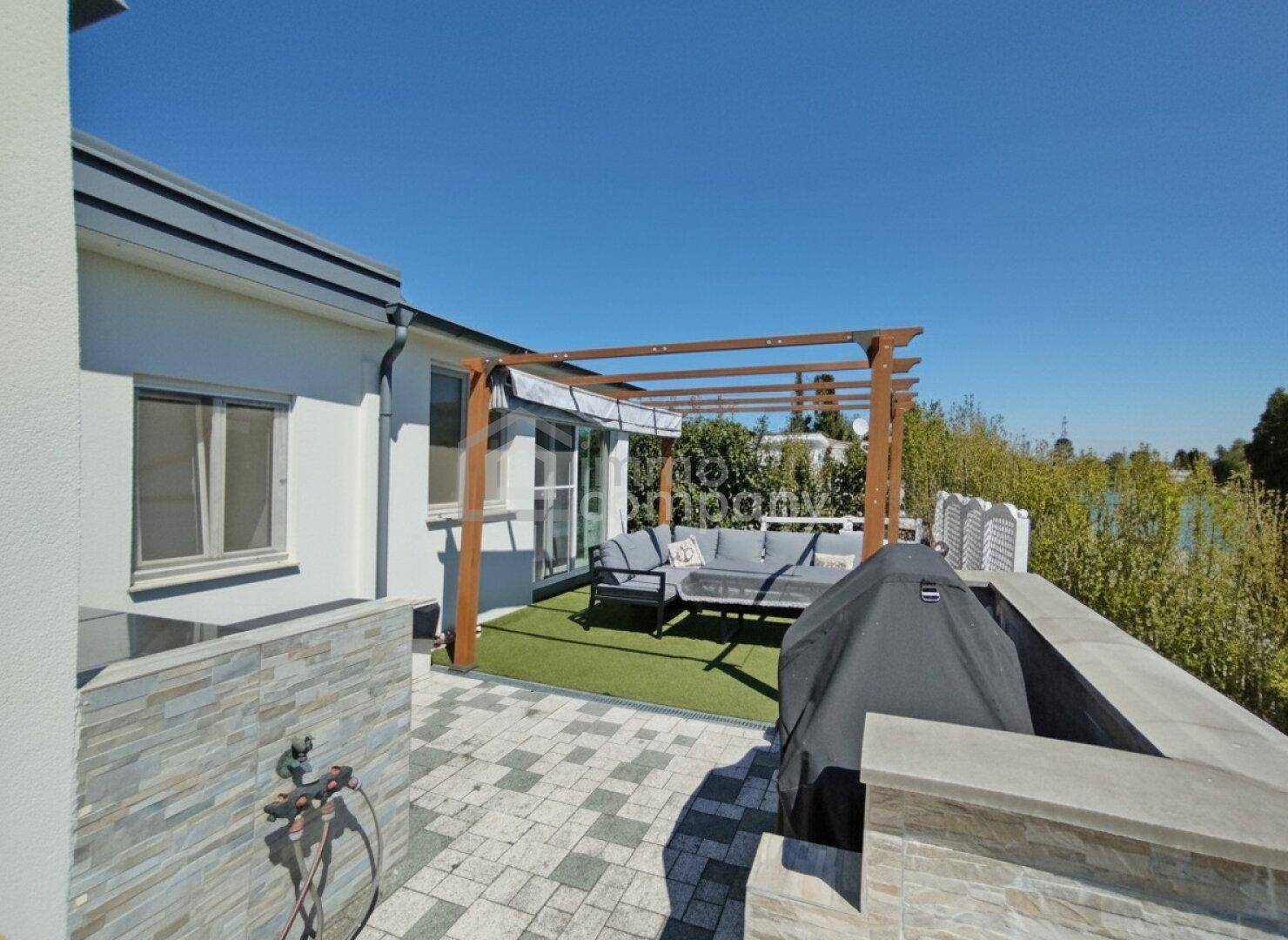 Moderne Terrasse mit Pergola, Lounge-Möbeln und Grillbereich, ideal für entspannte Stunden am Wasser.